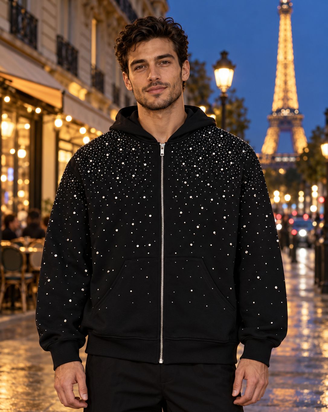 Homme portant le sweat zippé à strass EYDIZ noir devant la tour Eiffel, de nuit